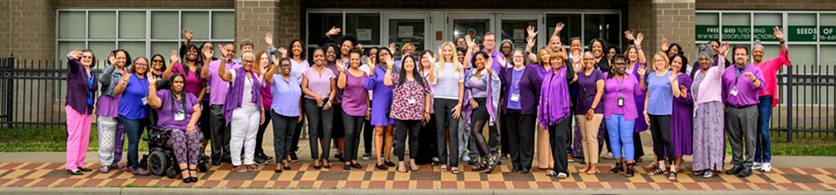 group of people wearing purple waving in front of a building