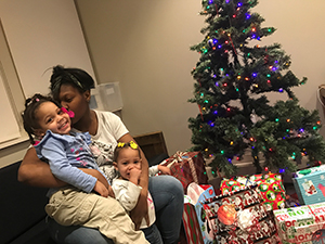 woman sitting by a Christmas tree hugging two children