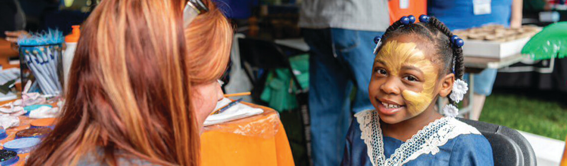 Woman painting child's face while child smiles