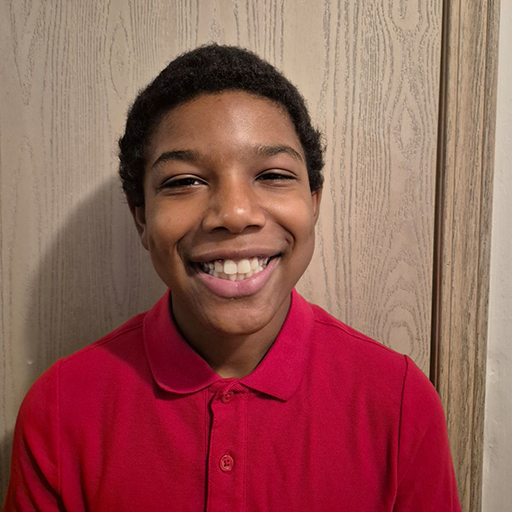 young man standing against a wall in a red shirt and smiling