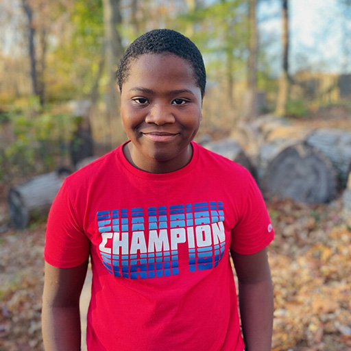 young man standing in a park with trees behind him and smiling