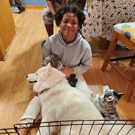 young woman smiling and petting a cat with a dog on her lap